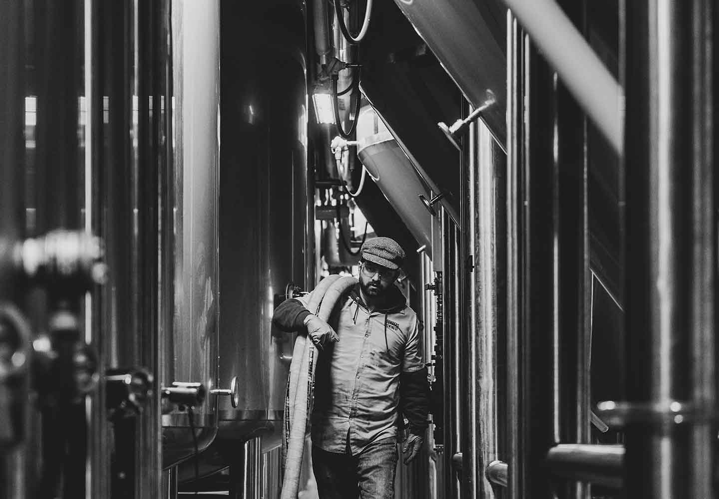 Black and white image of Founders employee carrying a hose in the Barrel House